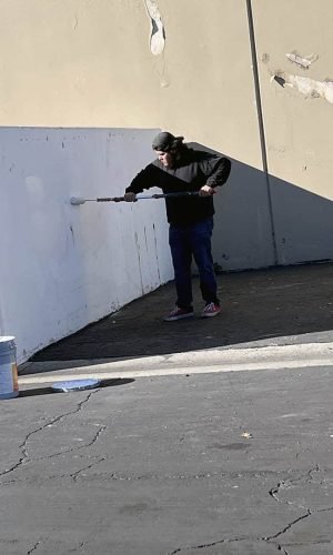 Man pressure washing a large outdoor wall with a high-pressure hose in California.