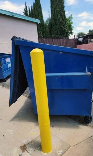 Blue dumpster with yellow safety post for waste disposal in an outdoor urban environment.