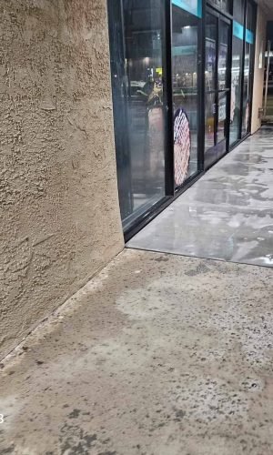 Pressure washing concrete sidewalk and storefront entrance in California.