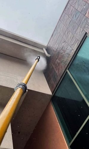 Professional pressure washing of building exterior with high-pressure water jet.