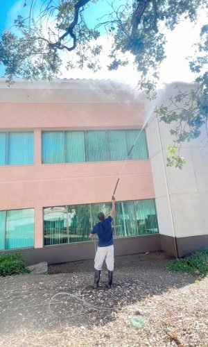 Professional pressure washing of building exterior with high-pressure water spray.
