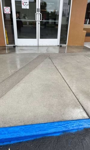 Commercial building entrance with clean concrete sidewalk and blue painted curb.