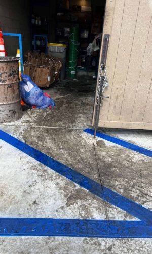 Garage floor being pressure washed with blue tape markings for cleaning in California.