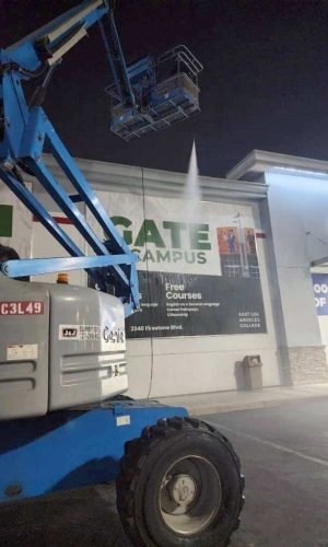 Pressure washing lift cleaning storefront exterior at night.
